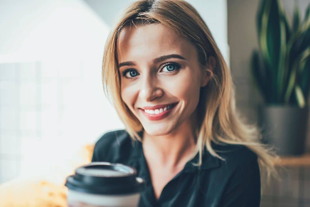 Smiling white woman holding coffee cup for teeth whitening