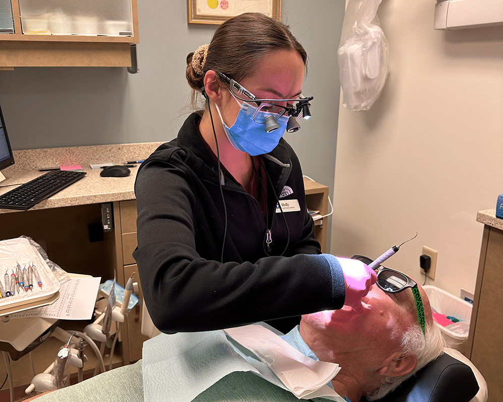 Holly dental hygienist cleans a man with white hair teeth and wearing sunglasses