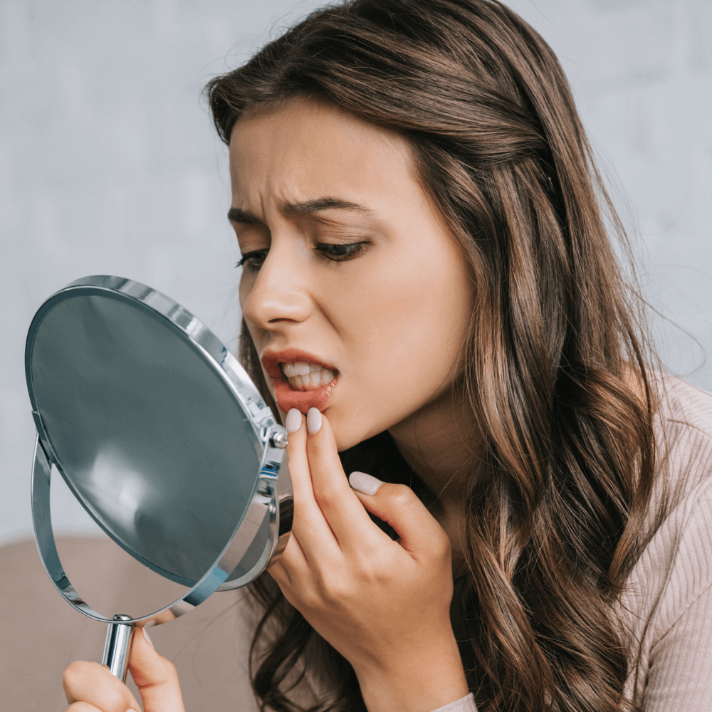 Woman looking in the mirror at mouth because it hurts. Seeking a emergency Dentist