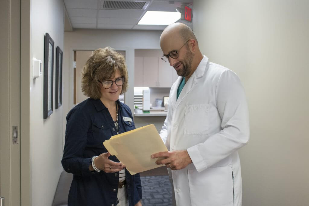 Two people in a hallway of a health clinic discussing a patient chart together. Man and woman; office manager and doctor